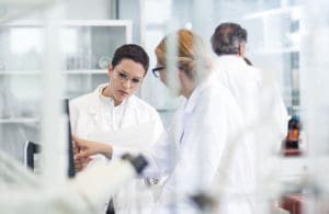A stock image showing two women scientists in lab coats, looking at a screen