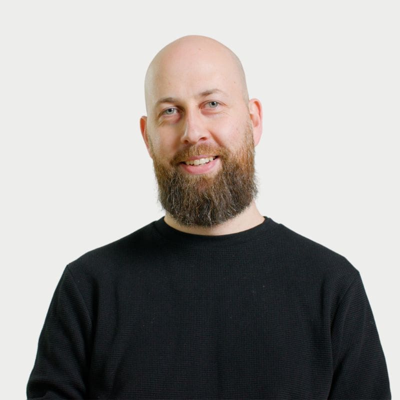 A head and shoulders shot of a man with no hair and a beard wearing a black tee shirt