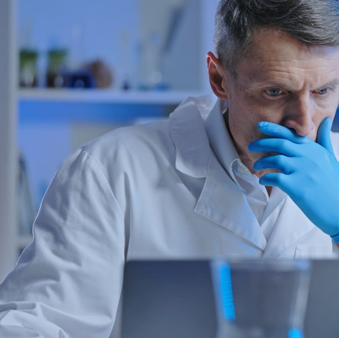 A worried looking man in a lab coat and gloves