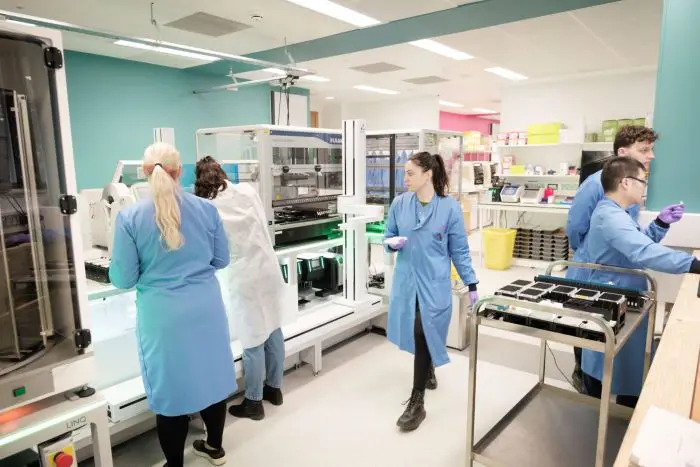 Five scientists in blue lab coats interacting with the instruments in their lab.