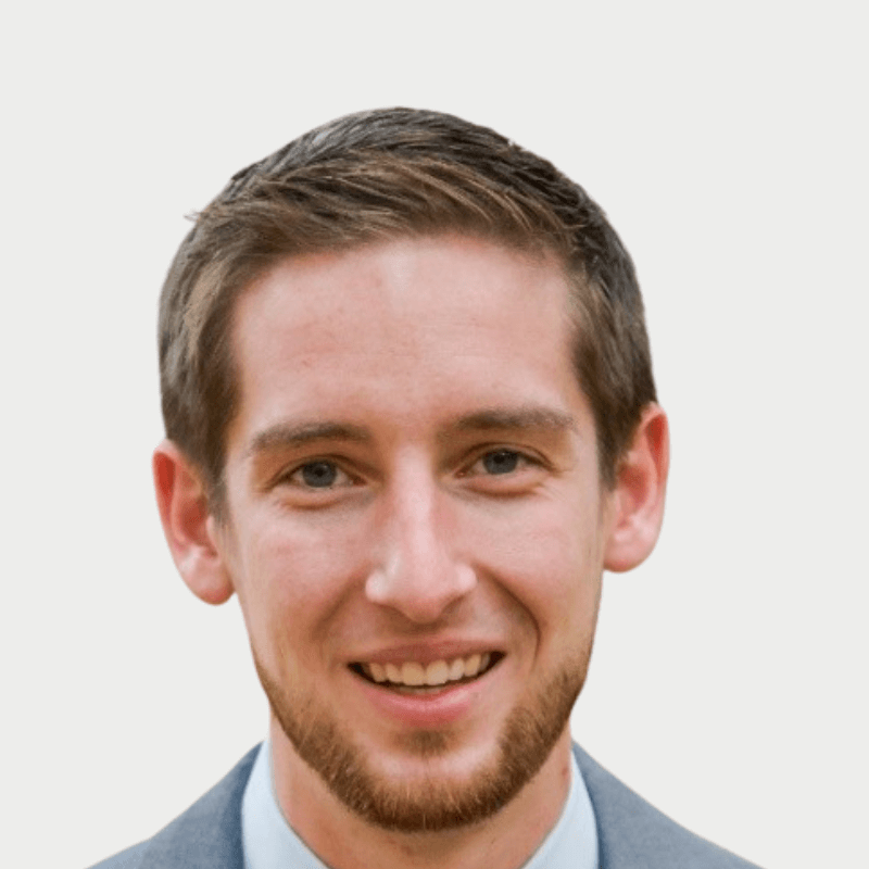 Head shot of a male with short brown hair and beard wearing a grey suit