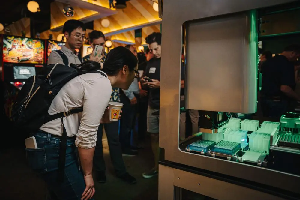 A woman looking at a liquid handling robot with a cup in her hand